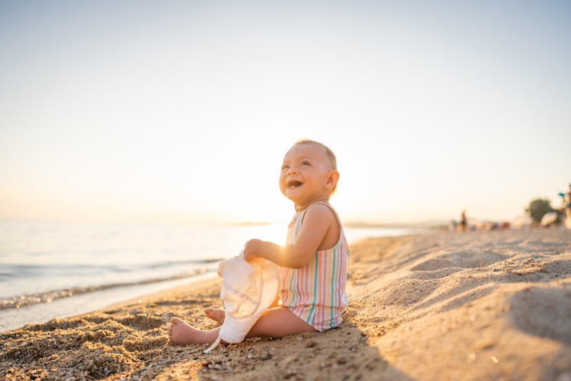 Baby girl with hat sitting at the beach in summer