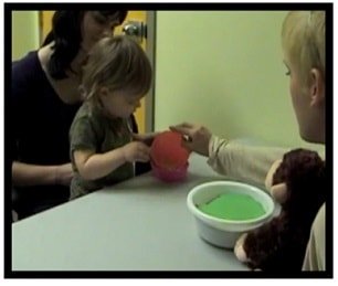 child receiving a bucket of treats from monkey puppet and woman