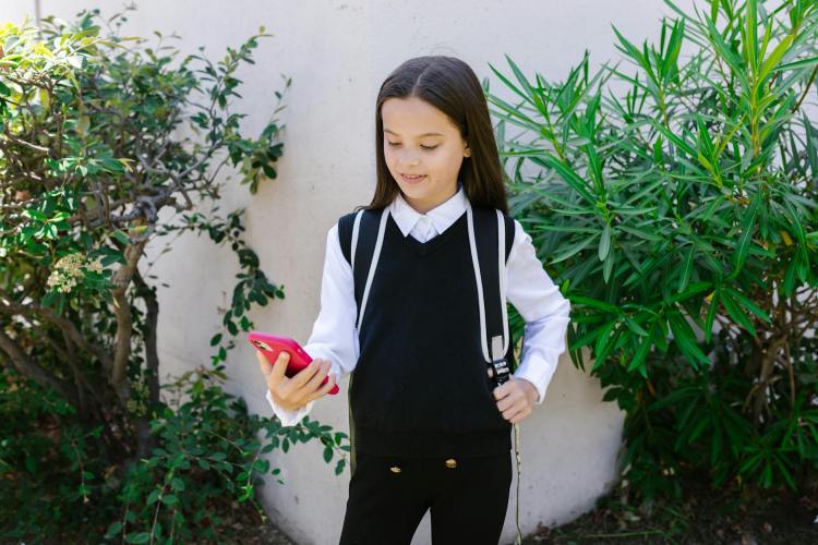 young schoolgirl with backpack holding pink phone