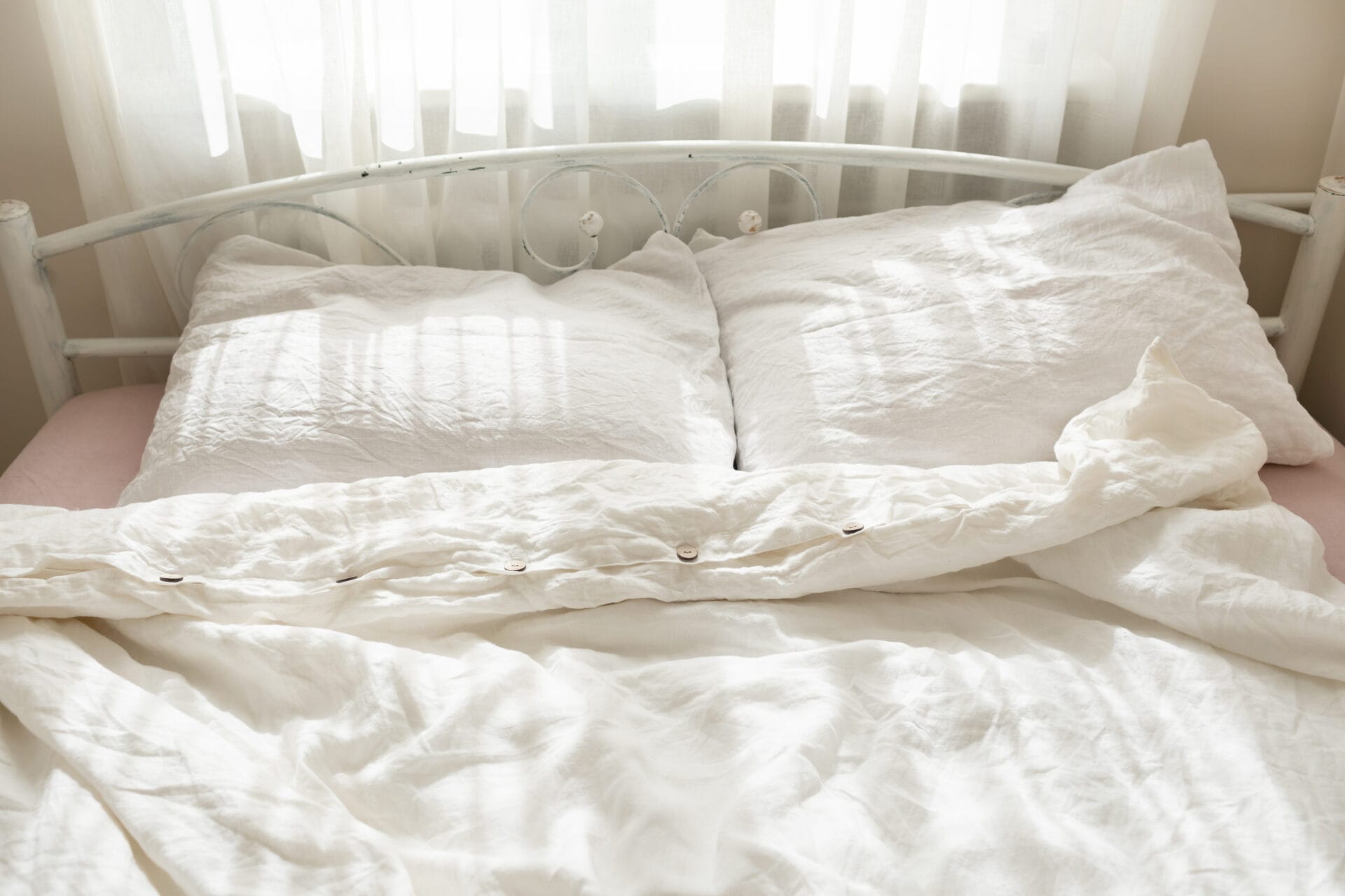 Beautiful morning light in bedroom. Pastel color white bedding. Trendy organic natural linen bedclothes. Cozy home interior.