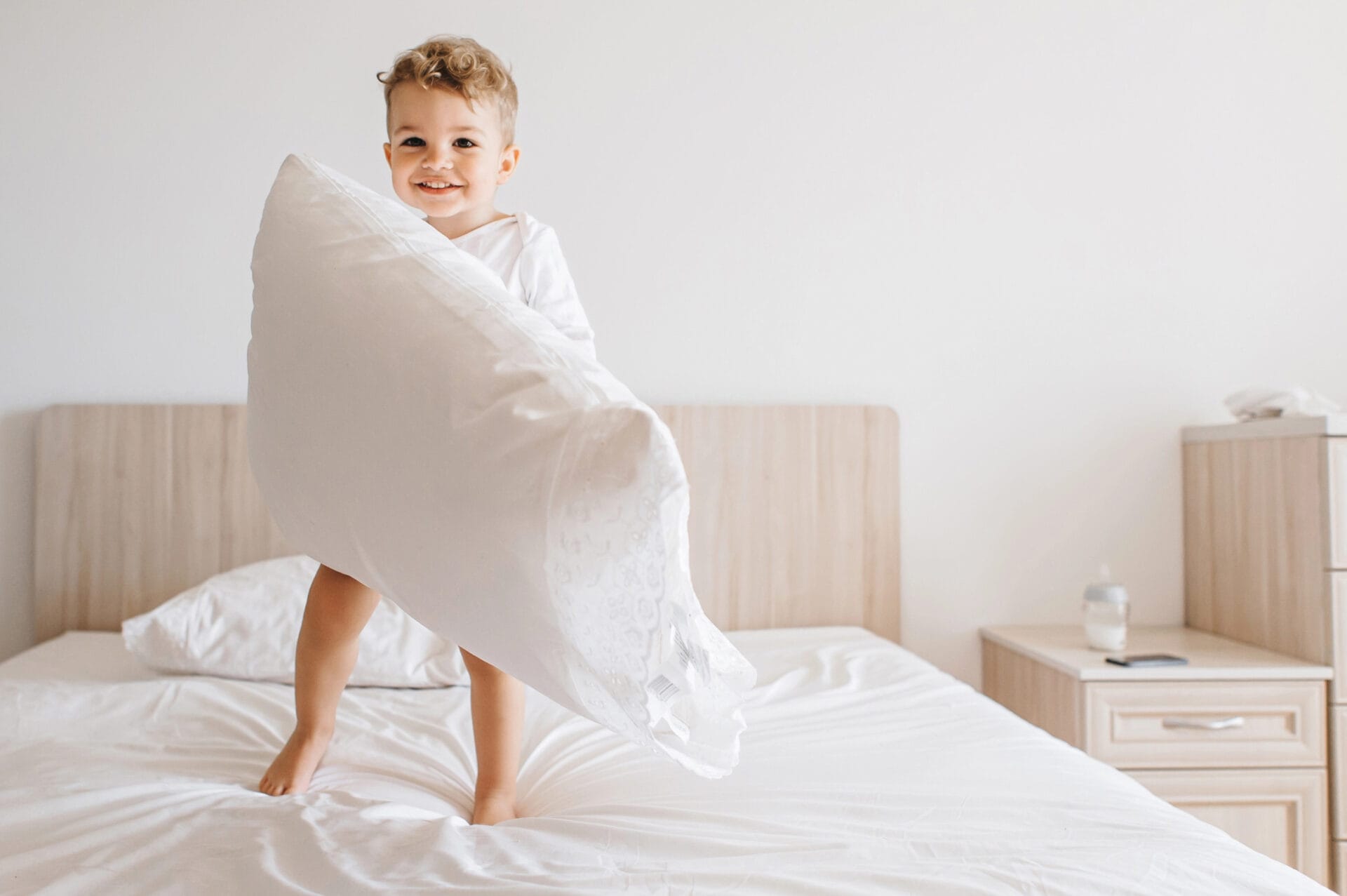 Adorable child jumping on bed holding organic pillow