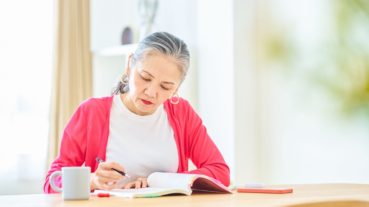 woman studying writes in notebook at a table.