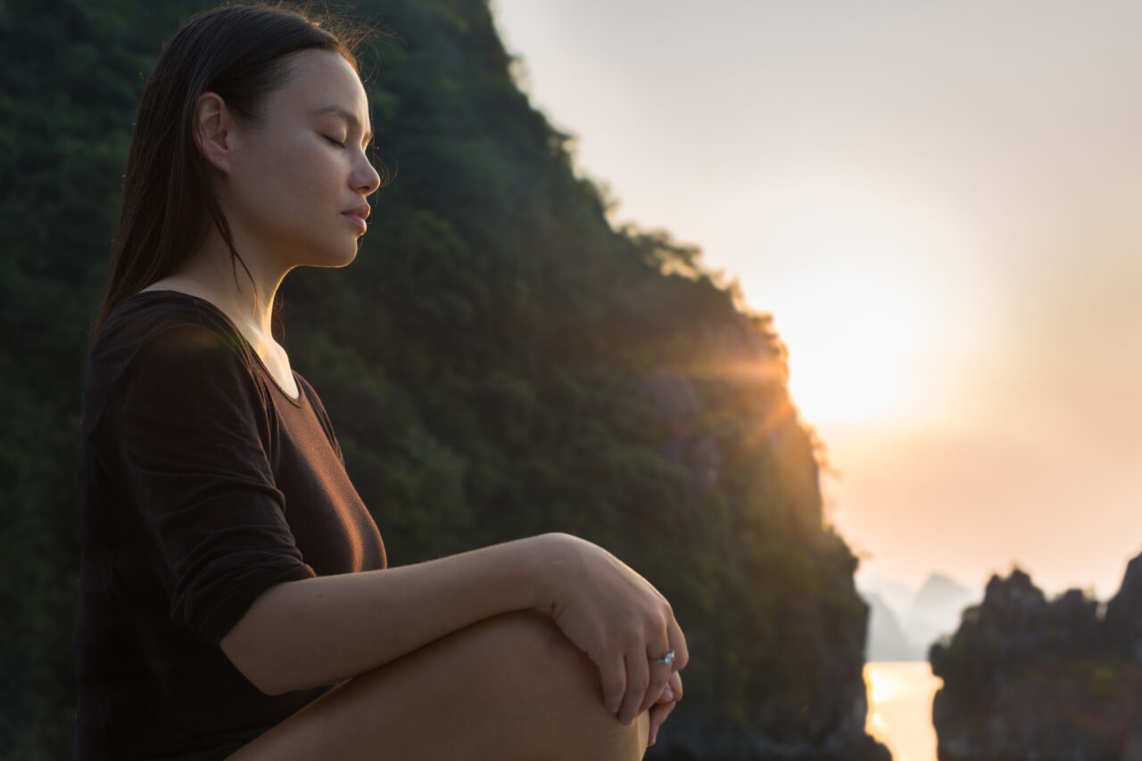 Woman relaxing and meditating in nature, during sunset.