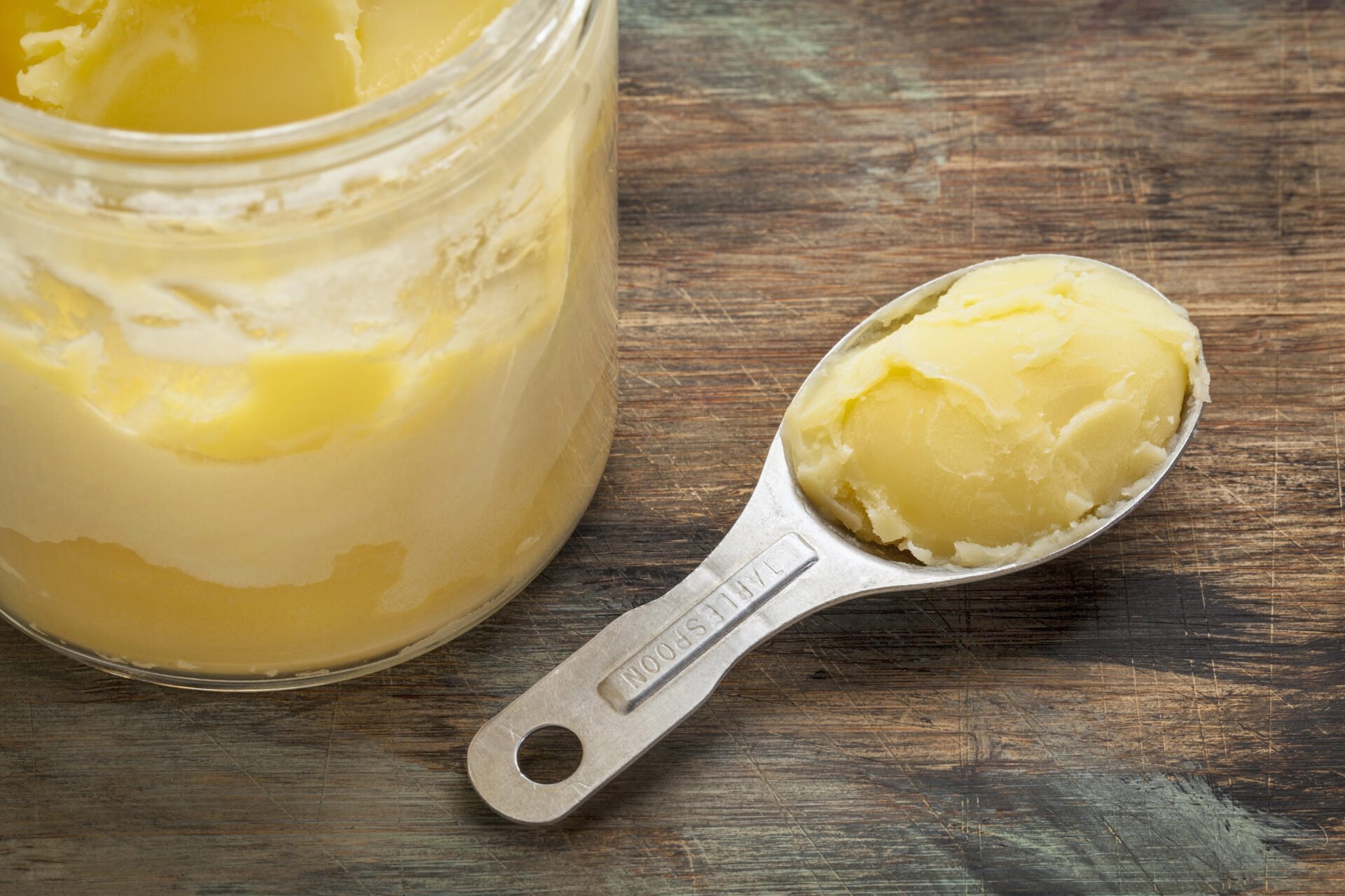 ghee on wooden table with stainless steel tablespoon