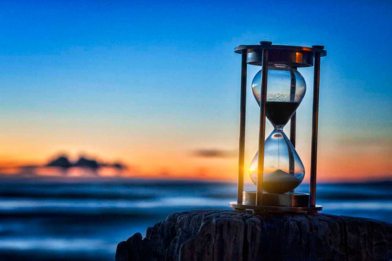 Hourglass or sand timer in front of a beautiful clear sunrise or sunset.