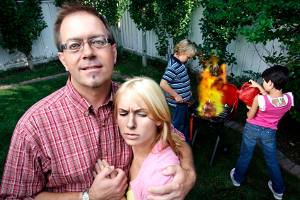 parents posing for photo in foreground, unaware that children are burning up the BBQ in the background