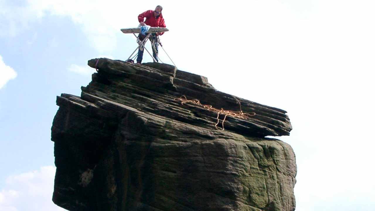 Man ironing shirt on top of cliff structure.