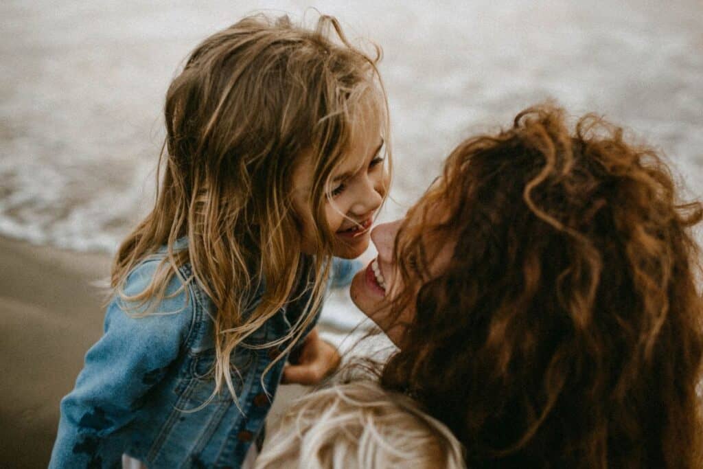 A mom looking into her daughters eyes on the beach, her son hugging her. 