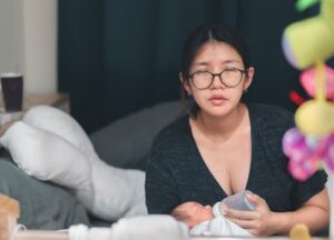 very tired mother, squints at viewer, while she bottlefeeds her newborn at night