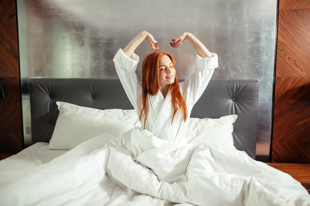 Redhead Woman stretching in bed after waking up, entering a day happy and relaxed after good night sleep