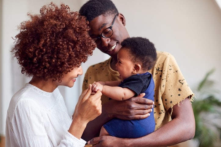 woman talking face to face with smilling baby while father holds him